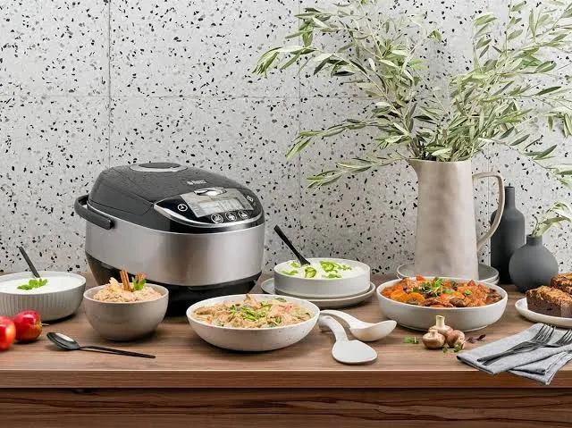 Multicuiseur électrique entouré de bols de riz et d'accompagnements servis